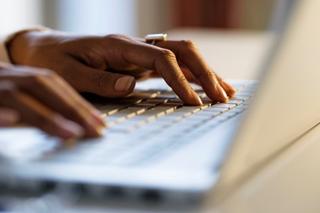 Image of a persons hands typing on a laptop keyboard