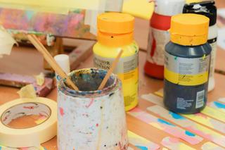 Close up of paint pots and bottles of paint in a Novus art class scattered across a table
