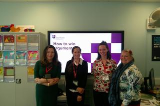 A group of female professors from Durham University stood in front of an interactive whiteboard in a classroom
