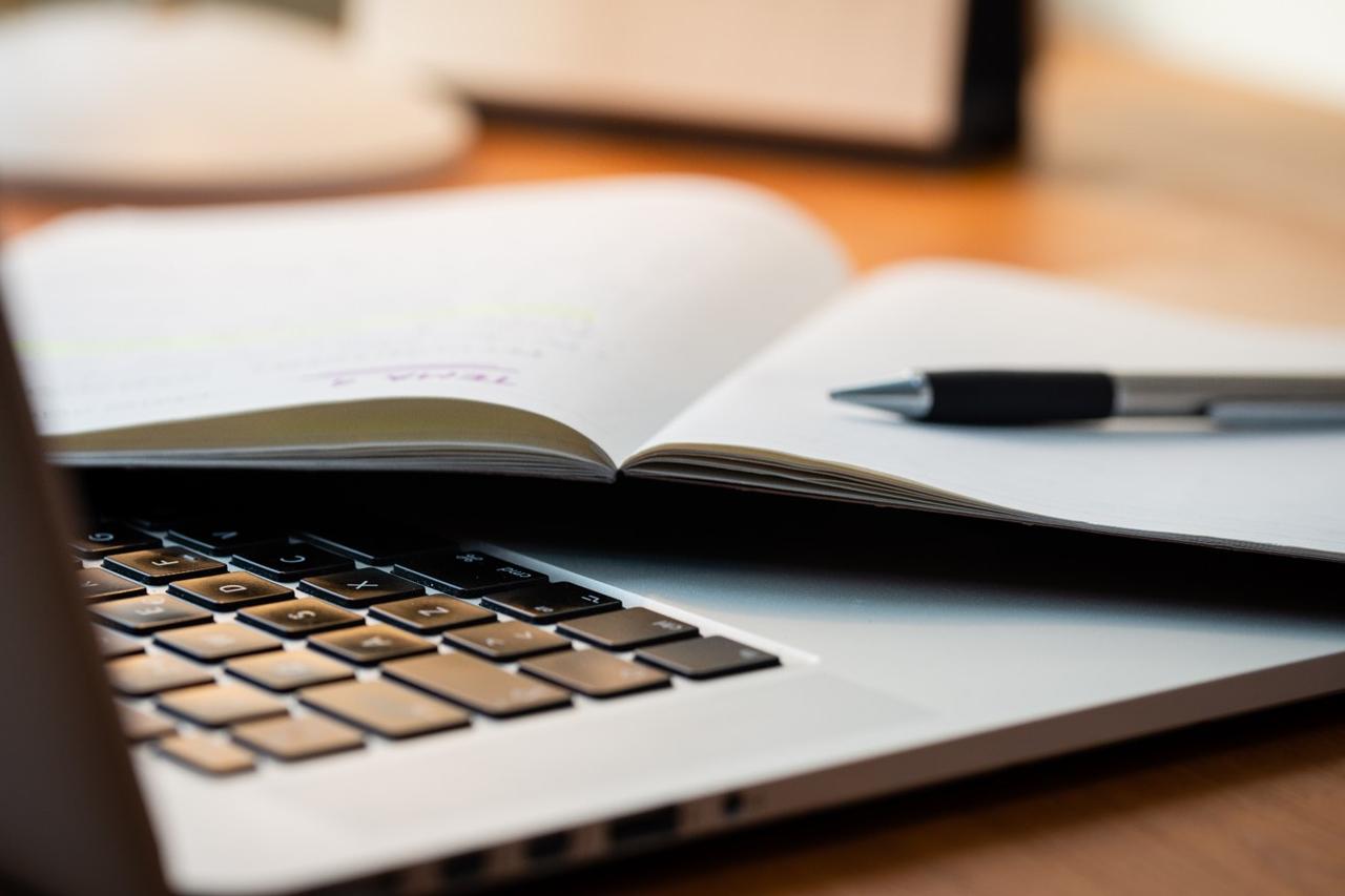 Close up of a notebook and pen resting on the keyboard of a silver laptop