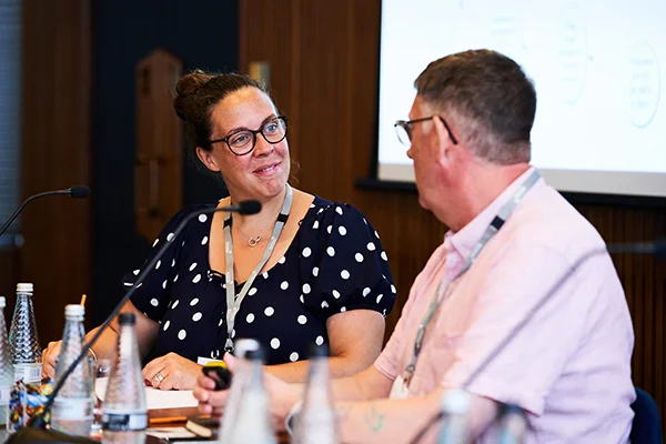 Two people engaged in conversation, focused on each other, with a blurred background, representing the 'quality team' role in prison education.
