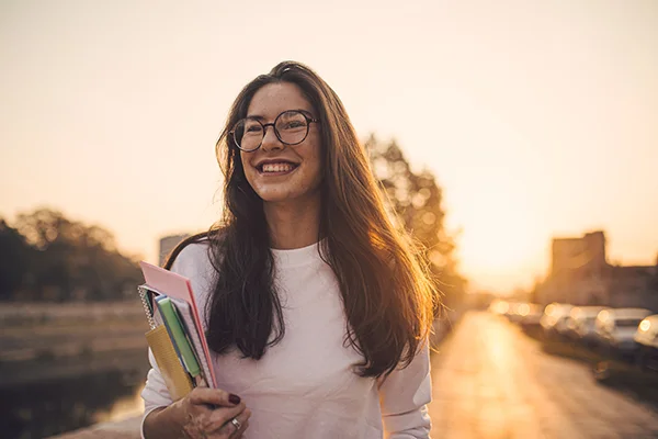 Smiling woman walking outdoors with books in her arms, representing a balanced and fulfilling work-life experience.