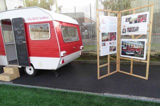 A red caravan parked next to a poster board