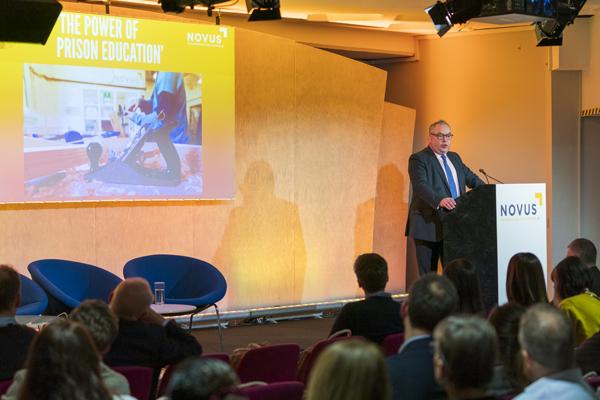 Speaker addressing an audience about Novus’ work in prison education and vocational training.