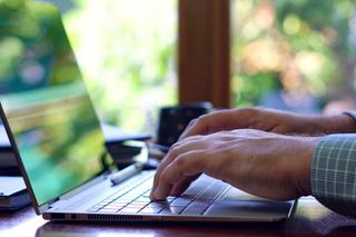 A man typing on a laptop, sat at a desk