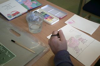 A man painting a picture of Peppa Pig that he's copying from a Peppa Pig storybook