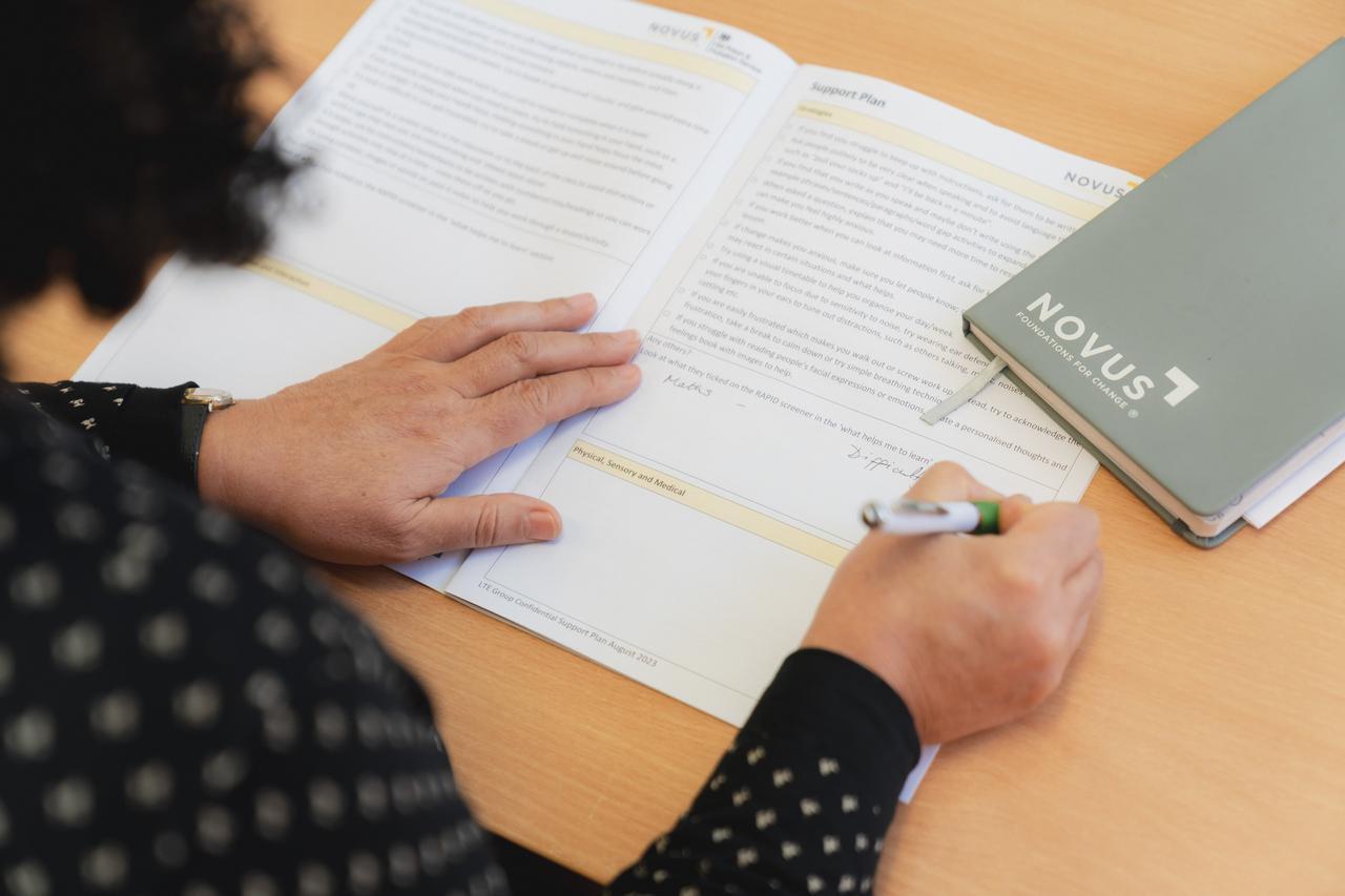 A learner support plan being completed during an educational assessment, with Novus learning materials visible on the desk at HMP Styal