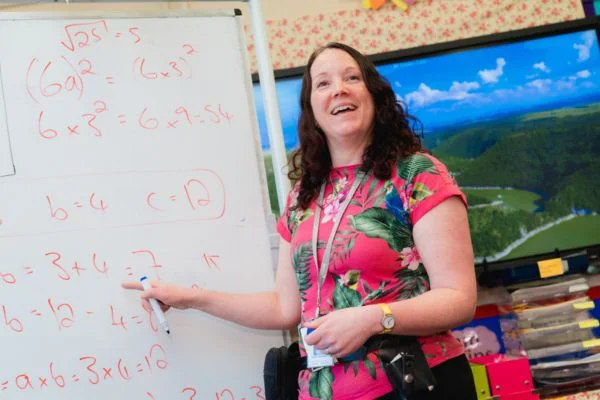 Novus prison teacher smiling and pointing to whiteboard with written calculations on