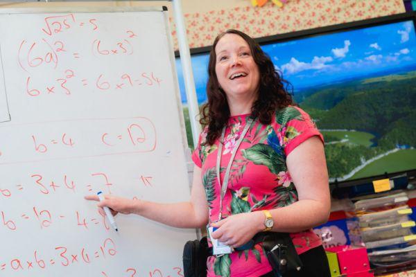 Novus prison teacher smiling and pointing to whiteboard with written calculations on