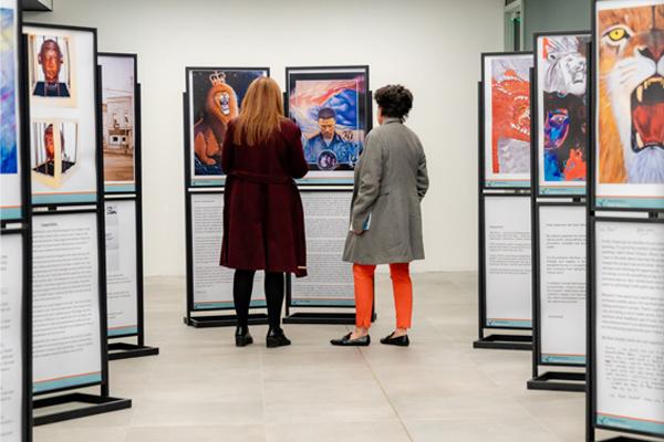 Two people viewing artwork in a modern gallery exhibition with framed displays.