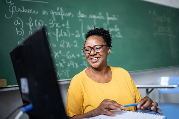 Smiling woman sitting in front of a chalkboard, representing the role of a Local Education Manager in prison education.