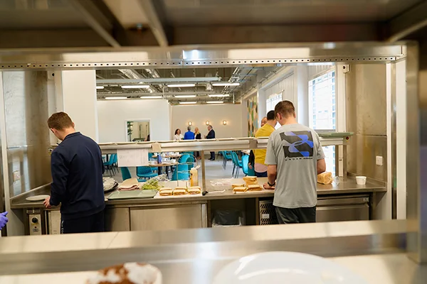 People working together in a canteen, serving food and engaging with each other, representing the 'Novus works team' role in prison education.