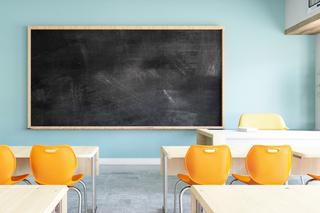 Empty classroom with desks and orange chairs facing towards the blank blackboard at the front of the classroom