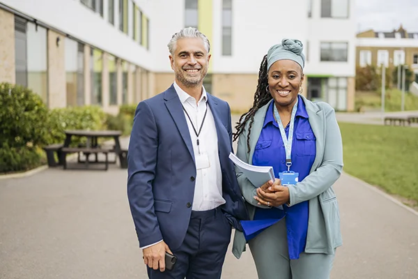 Smiling man and woman standing outside a building, representing the Lot/Senior Manager role in prison education.