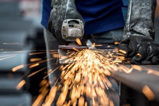 A worker in protective gloves welding with the tool he's using catching fire/sparking on the material on his work bench