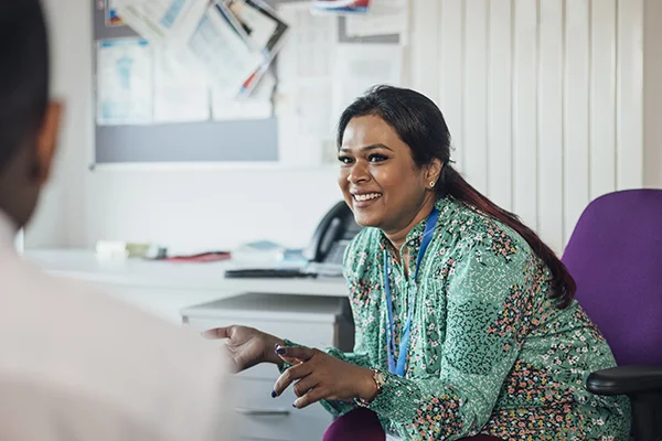 Over-the-shoulder view of a woman laughing and talking with others, symbolising the role and connection of a qualified teacher in education.