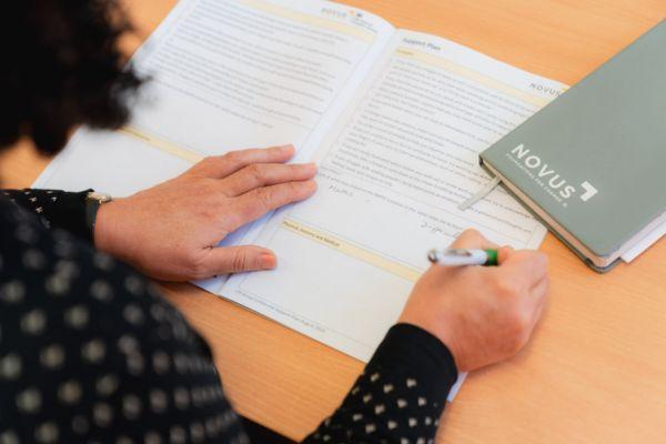 Person writing with a pen on a Novus learning plan