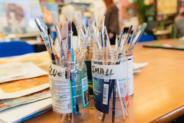 Jars of paintbrushes on a classroom table in an art studio setting.