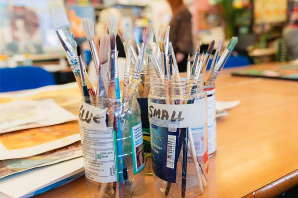 Jars of paintbrushes on a classroom table in an art studio setting.
