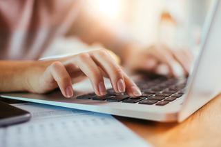 A close up of an individual sat at a desk typing on the keyboard of a laptop