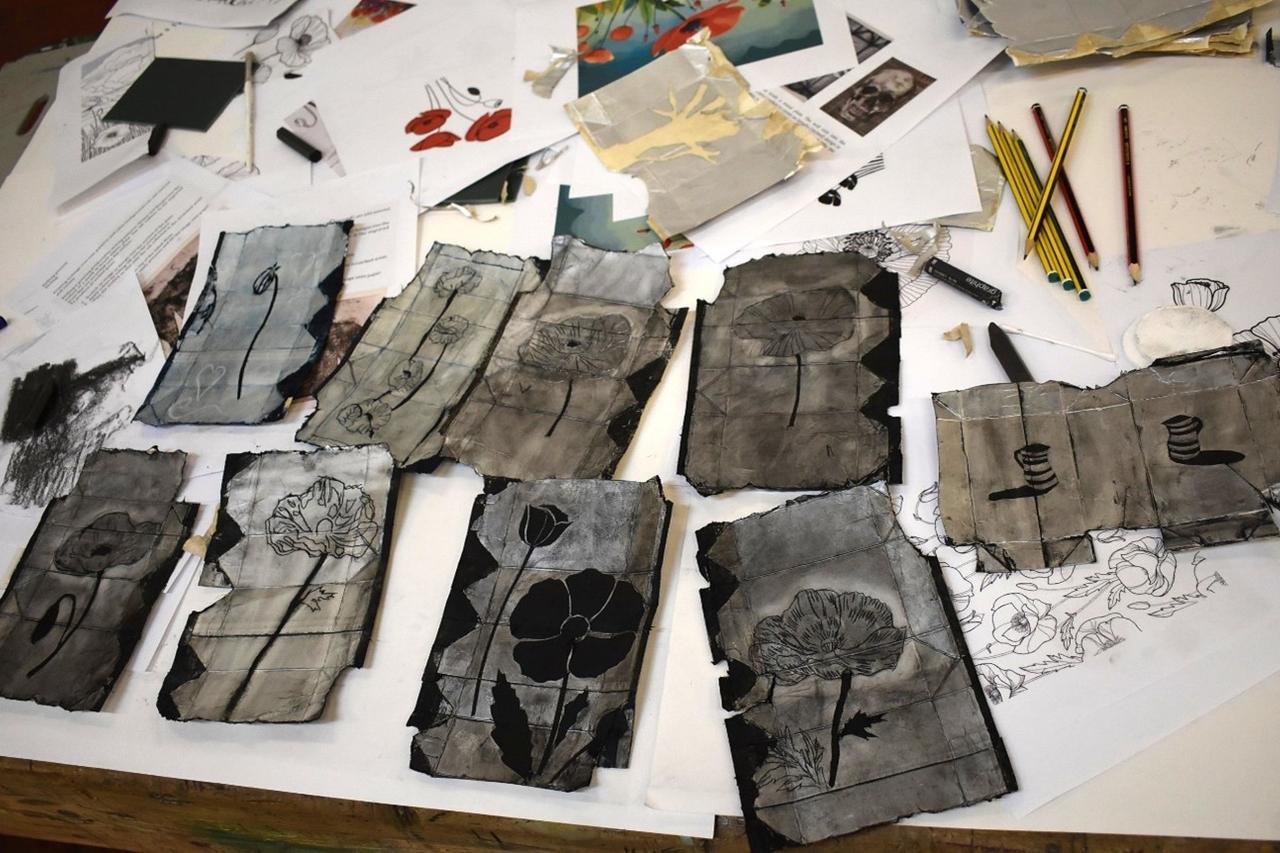 Printmaking artwork created during a prison creative workshop, showing floral designs etched onto recycled Tetra Pak cartons laid out on a table with drawing tools.