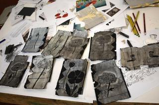Printmaking artwork created during a prison creative workshop, showing floral designs etched onto recycled Tetra Pak cartons laid out on a table with drawing tools.