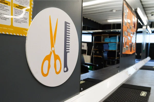 A close-up of a vocational training sign showing an orange pair of scissors and a comb, indicating a hairdressing or barbering provision area.