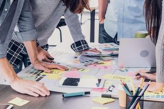 A group of colleagues working together around a desk with paper, pens and post it notes scattered over the table