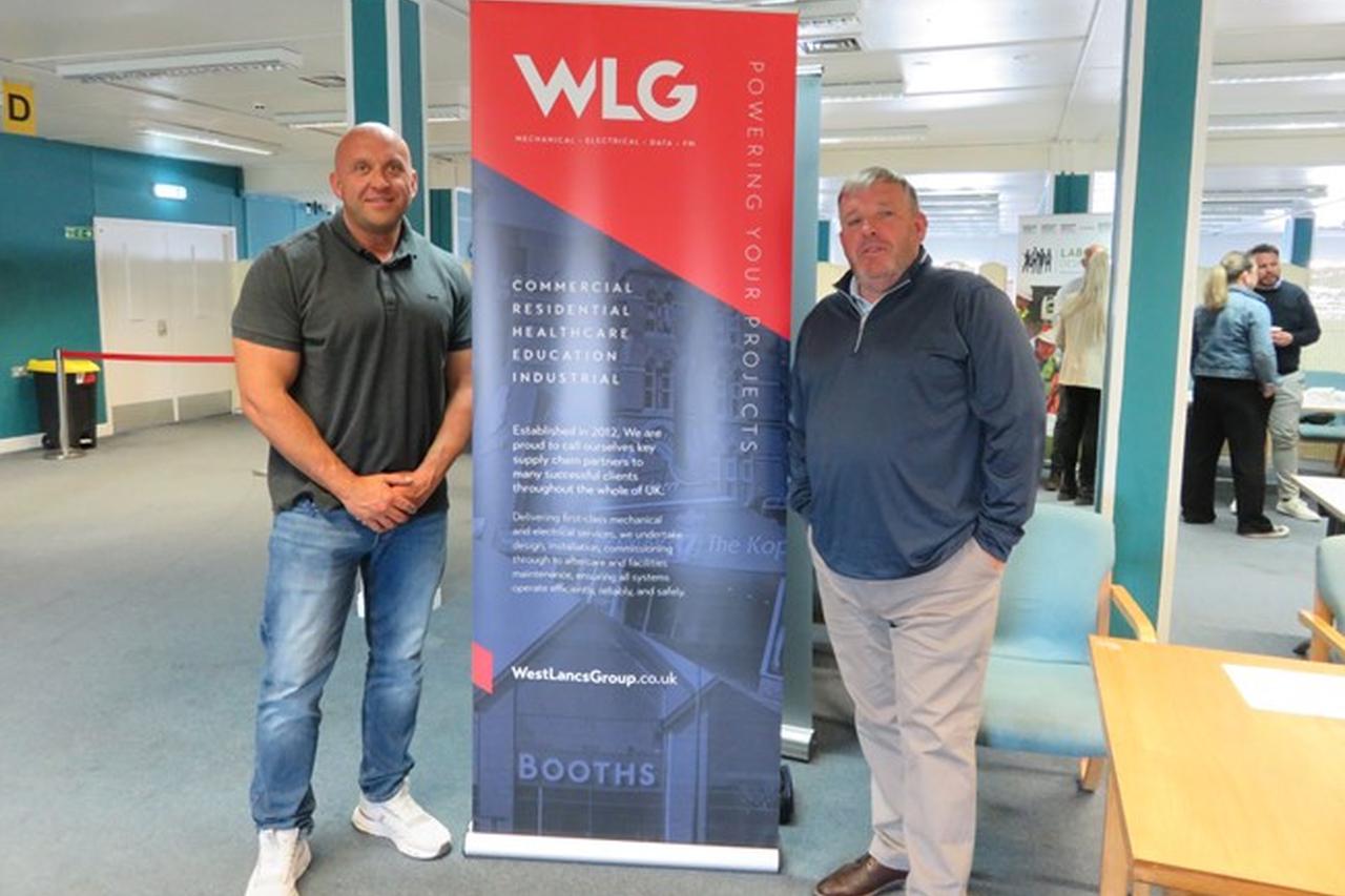 Two people from West Lancs smiling in front of their pull up banner at the employment event