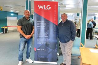 Two people from West Lancs smiling in front of their pull up banner at the employment event