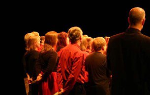 A group of people in a darkened room, singing.