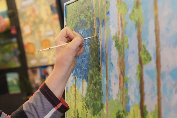 Close-up of a Novus adult learner painting on a canvas with a brush in an art class.