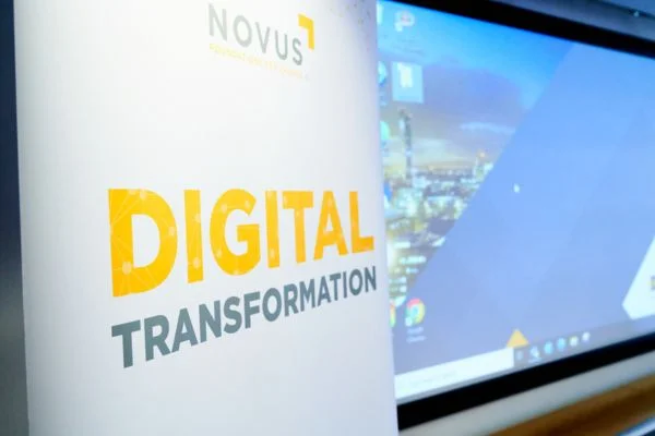 Sign in front of a screen that reads "Novus digital transformation"