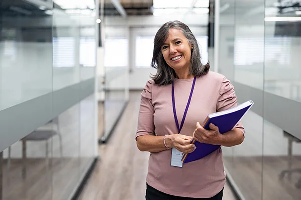 Smiling woman standing in a corridor, representing the 'Senco team' role in prison education, with a softly blurred background.