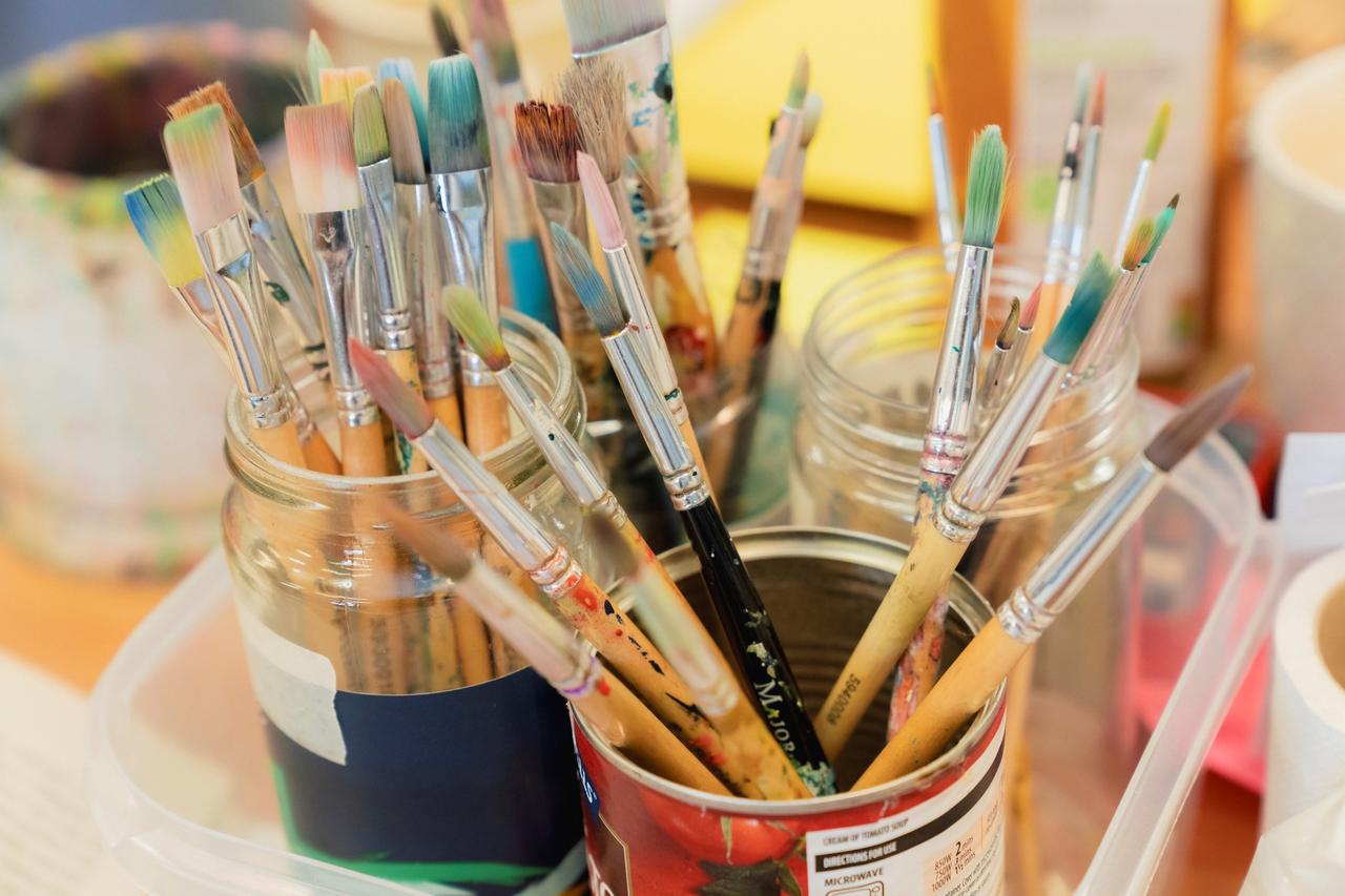An assortment of paintbrushes in paint pots on a table
