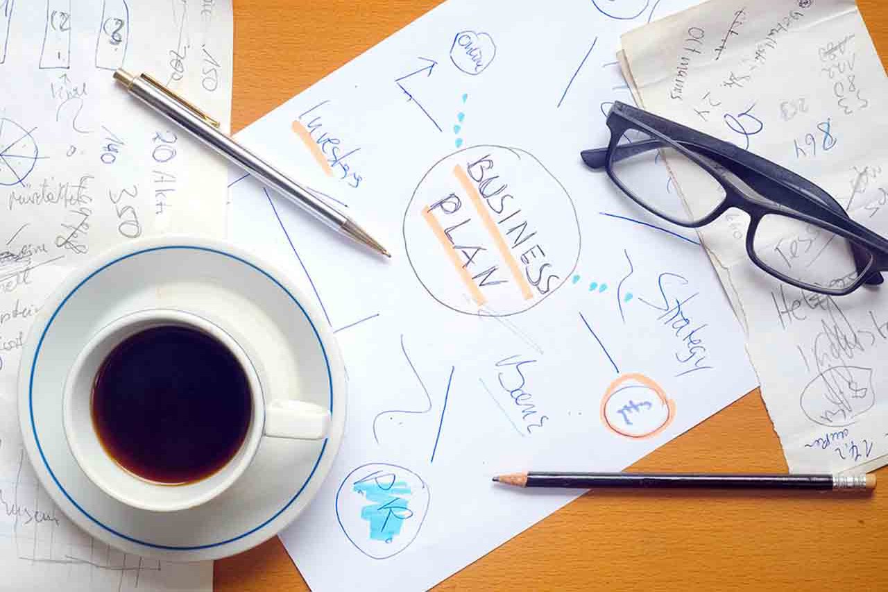 A desk with a business plan, coffee and glasses on