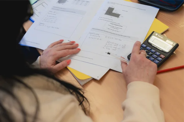 Over-the-shoulder view of a Novus tutor marking learner maths work using a calculator.