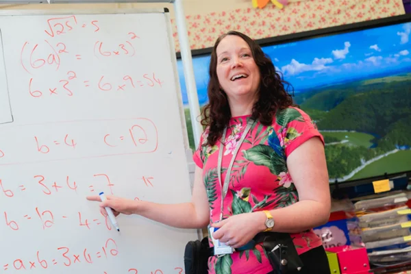 A Novus tutor smiling and pointing to a white board