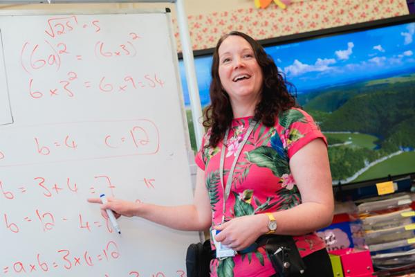 A Novus tutor smiling and pointing to a white board