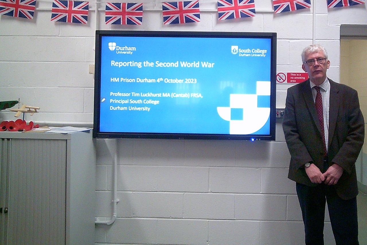 A history lecturer stood in a classroom, in front of a presentation about reporting in the Second World War