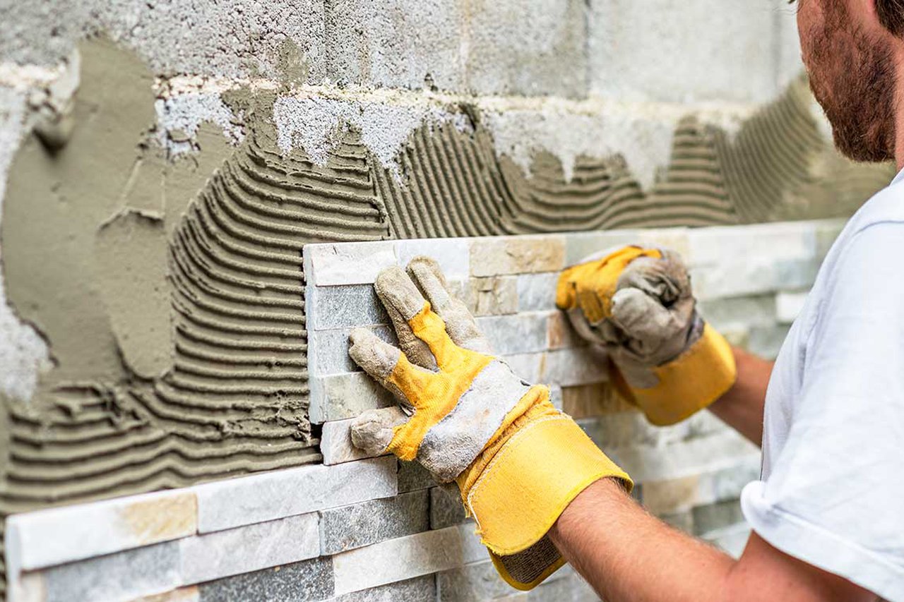 Over-the-shoulder view of someone tiling a wall